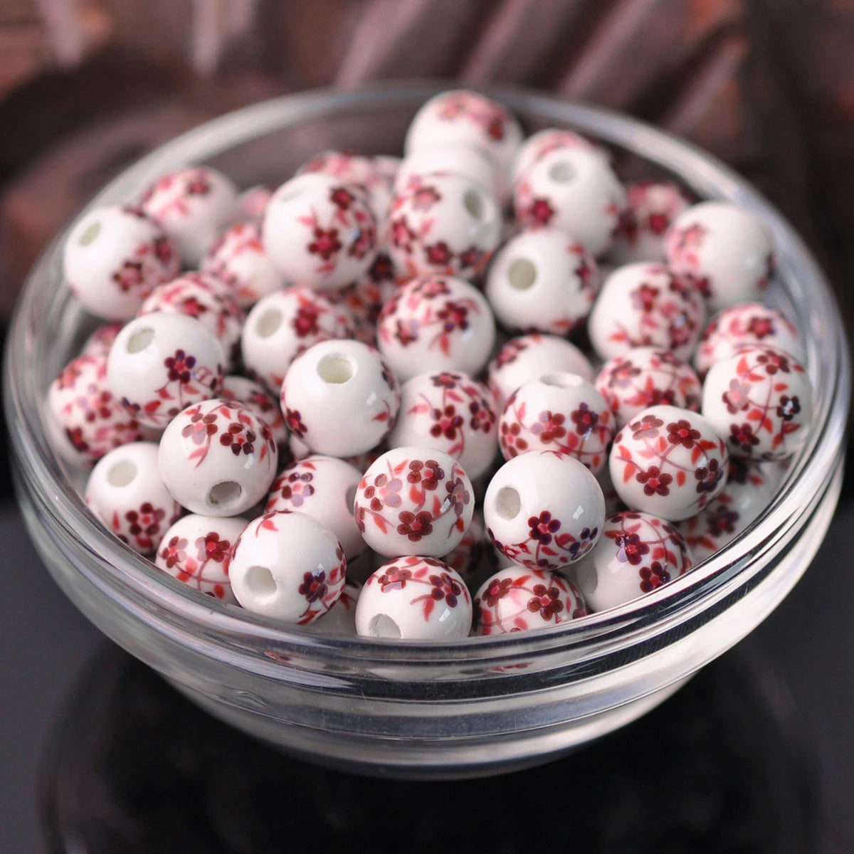 A clear glass bowl filled with small white ceramic beads decorated with red floral patterns.