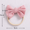 Pink knitted bow headband with a yellow elastic band shown flat.
