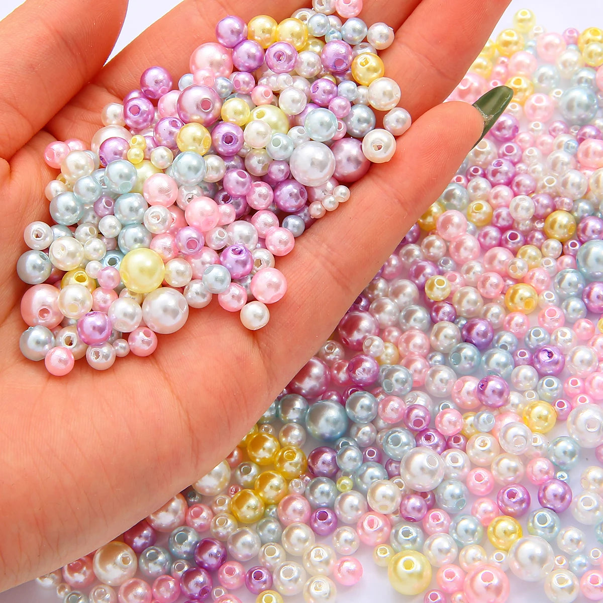 A hand holds a mix of assorted pink, purple, and white pearl beads for jewelry making.