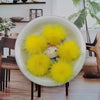 A white bowl filled with bright yellow soft mink fur pom poms for crafts and accessories.
