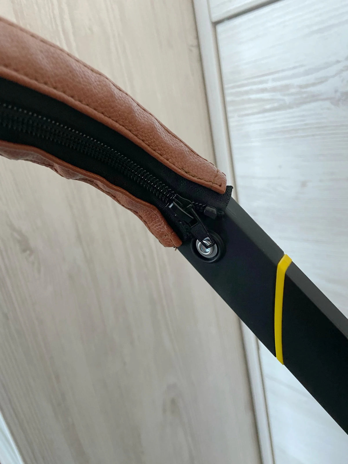A close-up view of a brown leather strap with a black zipper attached to a black pole, likely a stroller accessory kit.