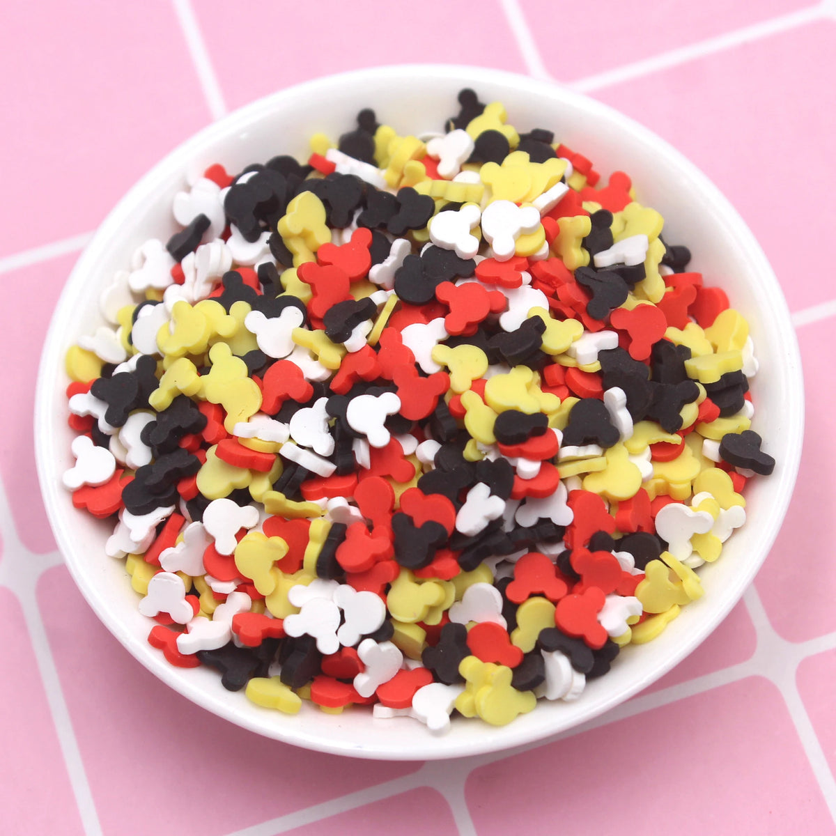 A bowl filled with multi-colored polymer clay slices in red, yellow, black, and white for slime and craft projects.