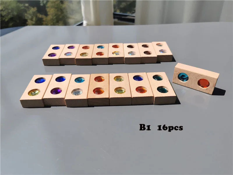 A set of 16 wooden gemstone building blocks with acrylic crystals arranged in two rows on a gray surface.
