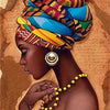 A close-up portrait of a woman with vibrant patterned headwrap and gold earrings, holding a painting tool.