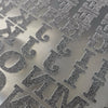 Close-up of DIY iron-on heat transfer patches for clothing with various decorative lettering designs on a gray surface.