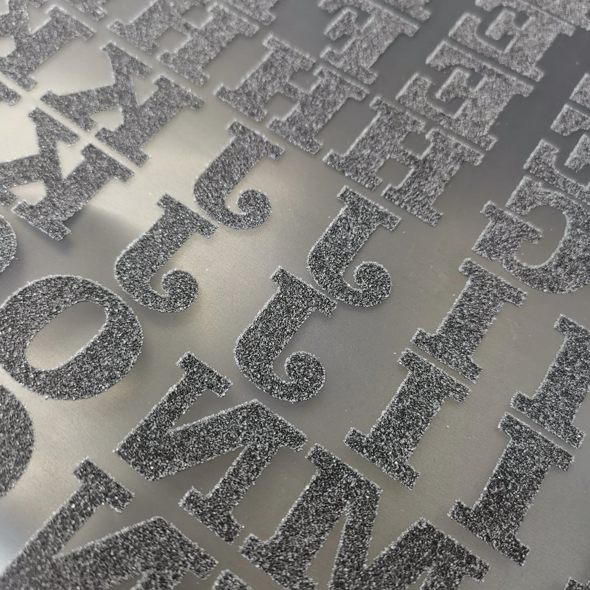 Close-up of DIY iron-on heat transfer patches for clothing with various decorative lettering designs on a gray surface.