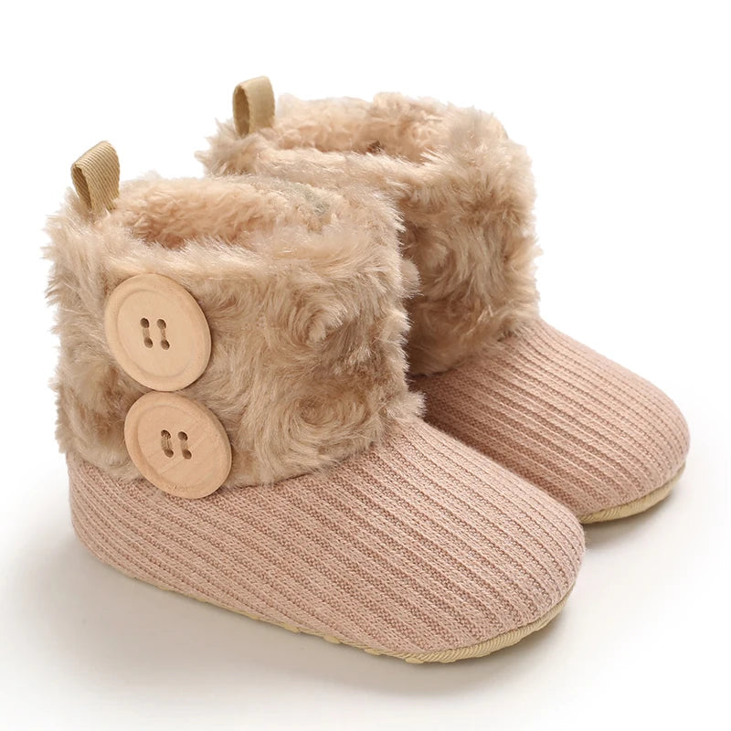 A pair of light beige plush baby snow boots with faux fur trim and wooden buttons.