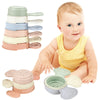 A baby is holding a set of boat-shaped stacking cups for bath time, featuring various pastel colors.