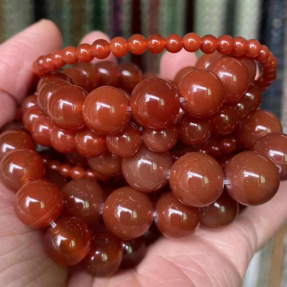A hand holds a strand of reddish-brown, spherical gemstone beads for jewelry making.