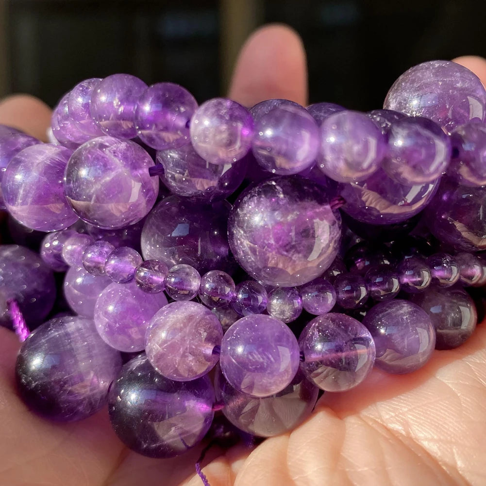 A hand holds a cluster of purple gemstone beads for jewelry making, including tiger eye and lava varieties.