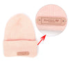 A pink knitted beanie with a leather-style handmade tag attached to the cuff.