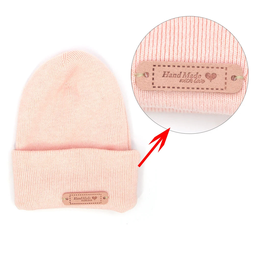A pink knitted beanie with a leather-style handmade tag attached to the cuff.
