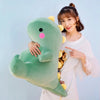 A woman is holding a large, soft green dinosaur plush toy against a light blue background.