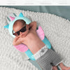 A baby is lying on a soft, light gray blanket using a pink and blue head protector pillow with an elastic strap.