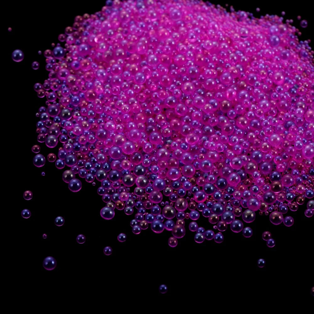 A pile of small, translucent pink and purple glass bubble beads for crafting.