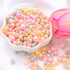 A pile of assorted pink, peach, and silver pearl beads is displayed next to a pink rose petal.