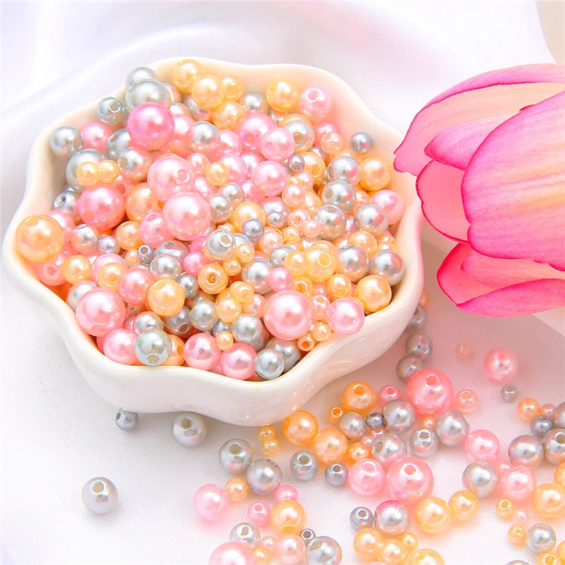 A pile of assorted pink, peach, and silver pearl beads is displayed next to a pink rose petal.