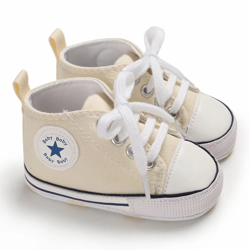 A pair of beige canvas baby shoes with white laces and a star-shaped tag for infants.