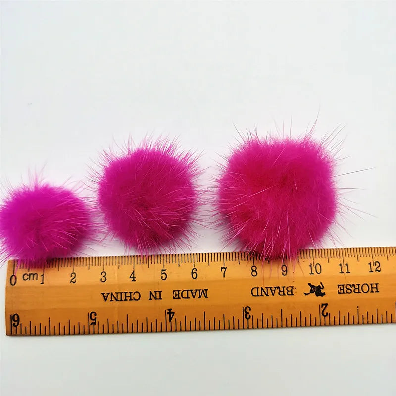 Three vibrant pink fluffy mink fur pom poms displayed next to a ruler.
