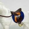A brown leather horse saddle and riding prop accessory is shown on a white horse figurine.