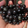 A handful of dark, polished gemstone beads including tiger eye and lava stones is held in a person's hand.