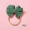 A teal green fabric bow headband with a light beige elastic band, photographed on a pink background.