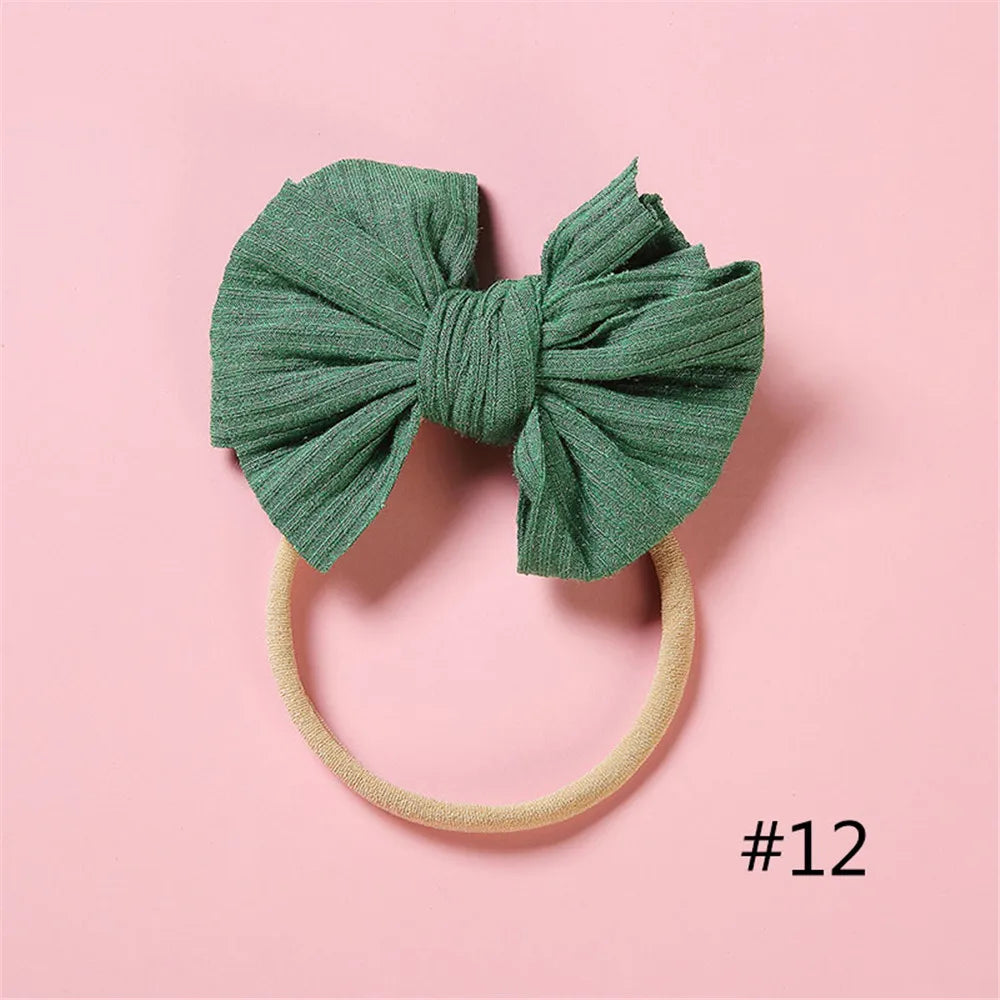 A teal green fabric bow headband with a light beige elastic band, photographed on a pink background.