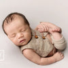 A newborn baby is lying down wearing a beige plaid vest and bundled in soft fabric, photographed in a studio setting.