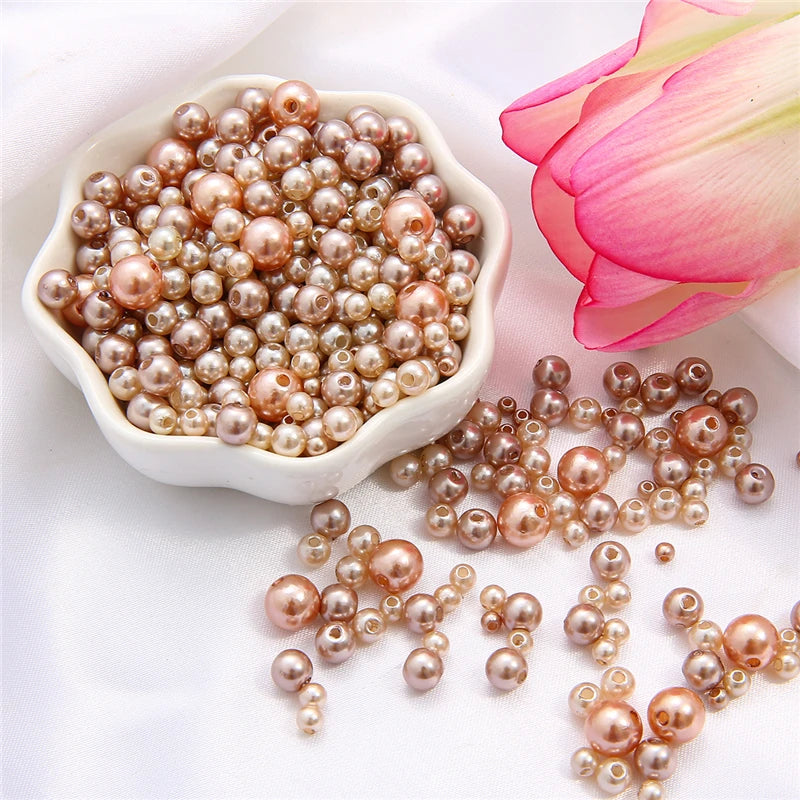 A pile of assorted pink and champagne colored pearl beads for jewelry making next to a pink rose flower.