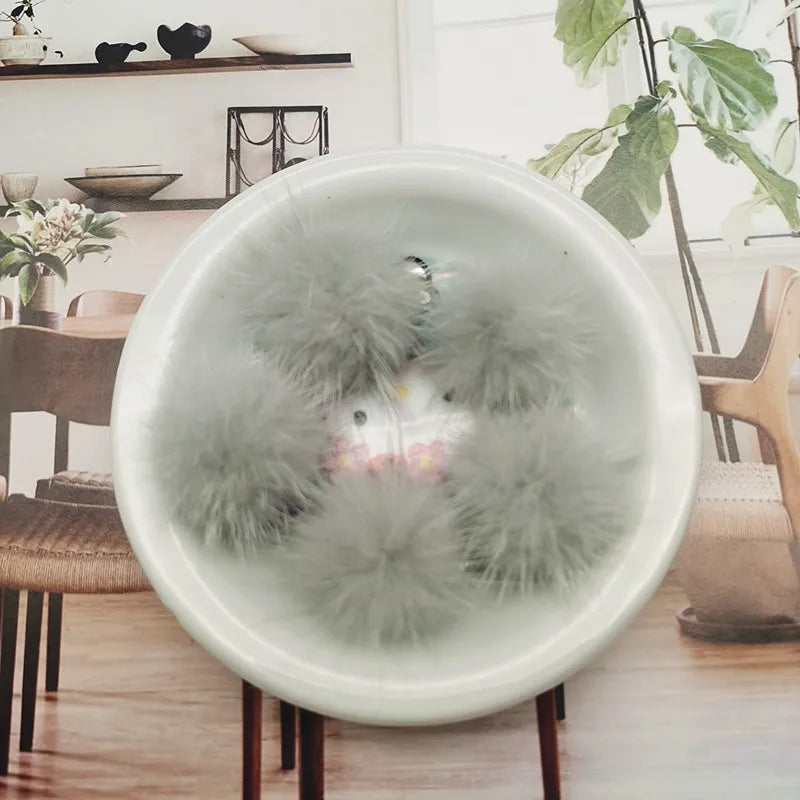 A white bowl filled with fluffy gray mink fur pom poms for crafts and accessories