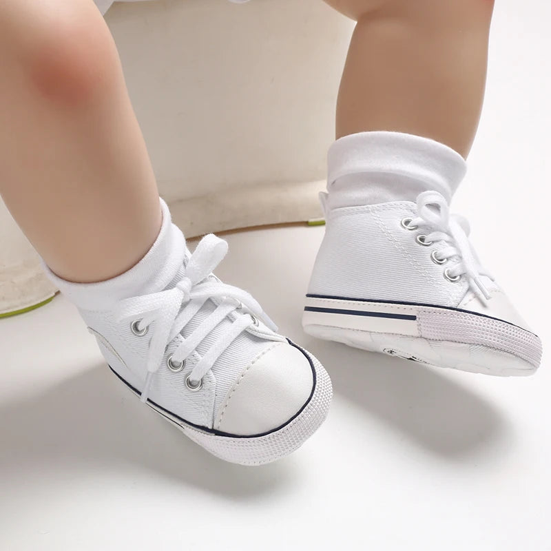 A pair of white canvas first walkers for infants shown from the side.