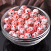 A clear glass bowl filled with small red and white floral ceramic beads for jewelry making