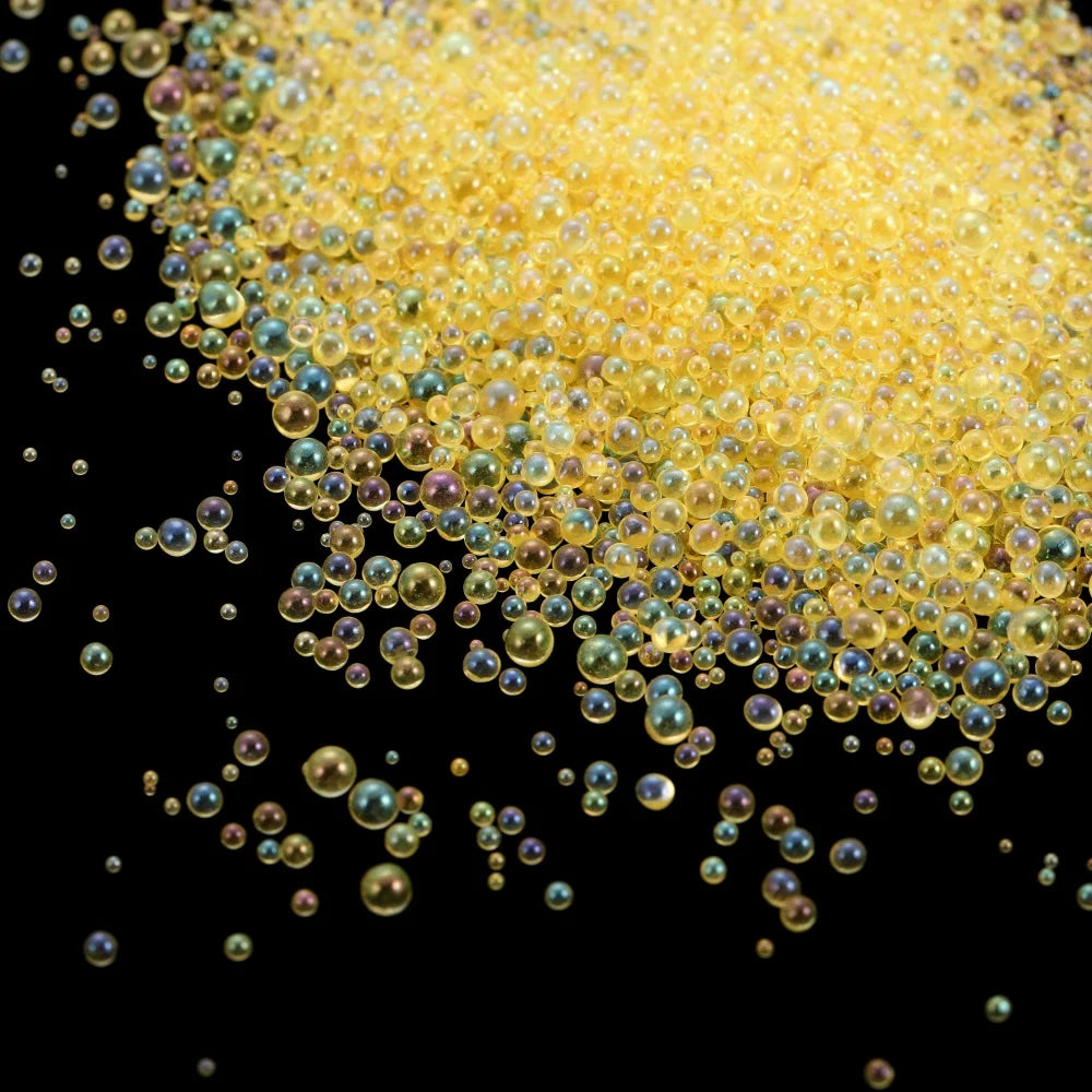 A pile of small, translucent yellow glass bubble beads scattered against a black background.