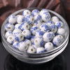 A clear glass bowl filled with small white ceramic beads decorated with blue floral patterns.
