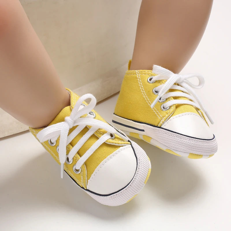 A pair of yellow canvas first walkers for infants with white laces and soles