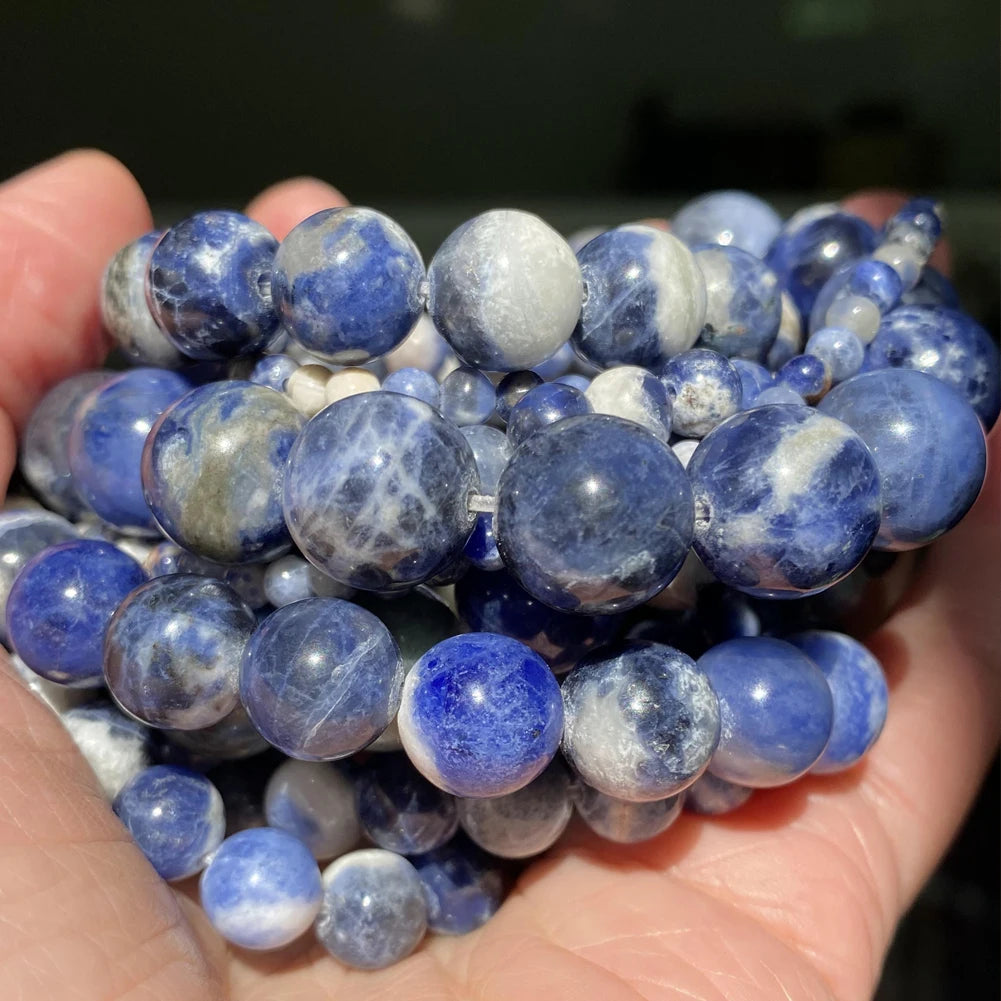 A handful of round natural gemstone beads in shades of blue and white are held in a hand.