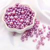 A pile of assorted purple and pink pearl beads for jewelry making displayed in a white bowl.