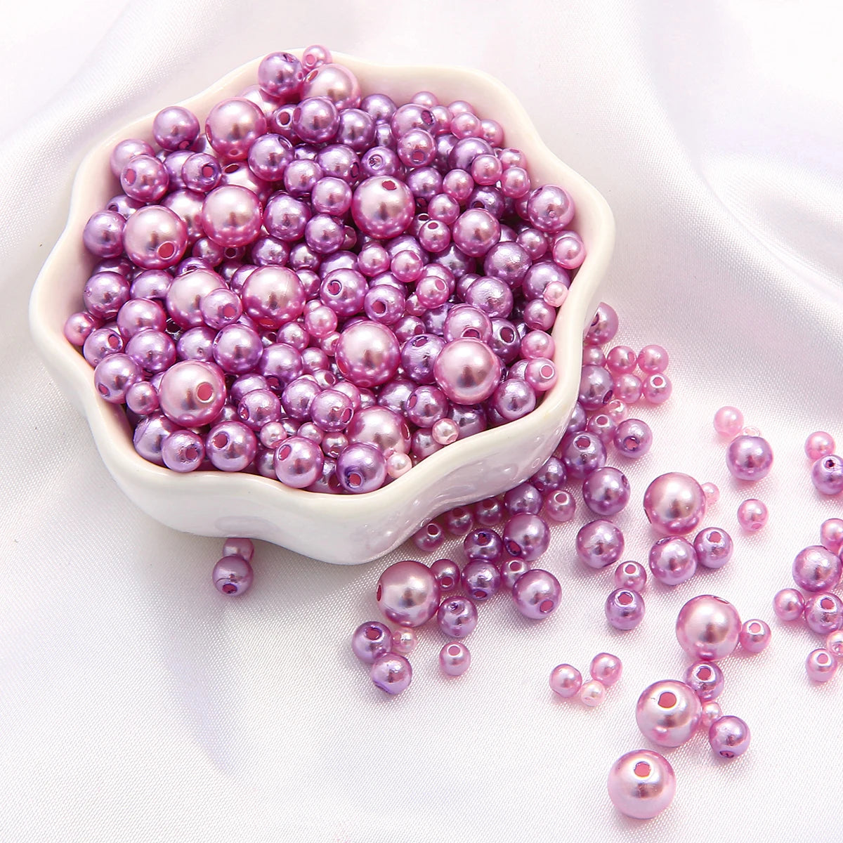 A pile of assorted purple and pink pearl beads for jewelry making displayed in a white bowl.
