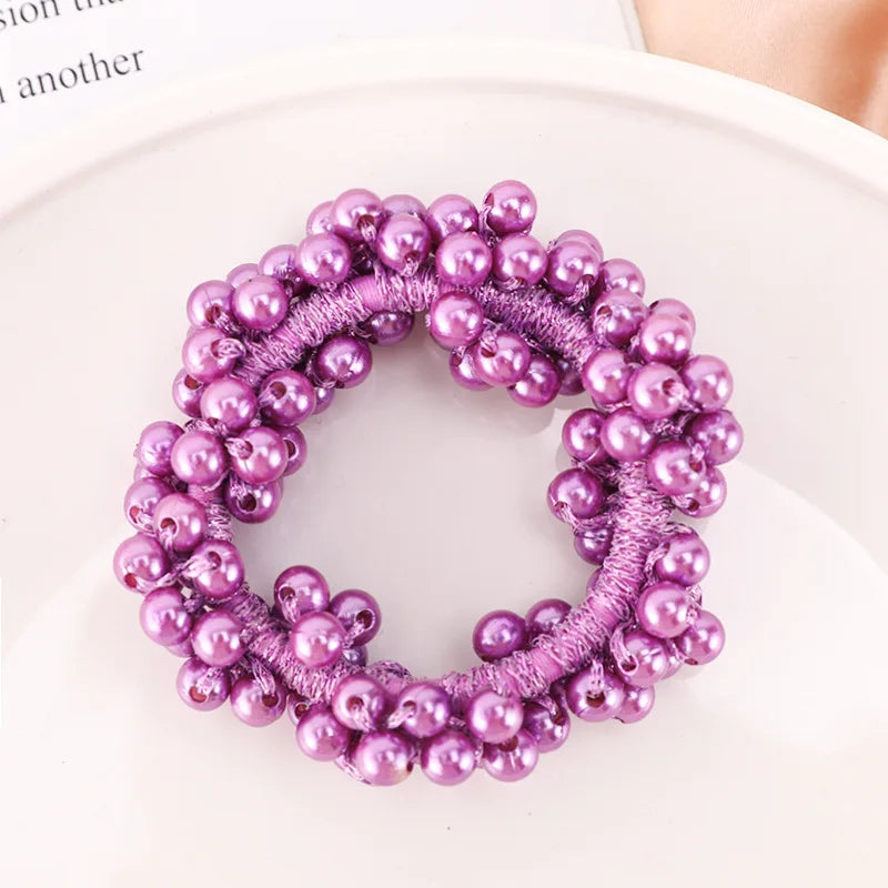 A circular hair accessory made of purple pearls and pink thread, resembling a bow scrunchie.