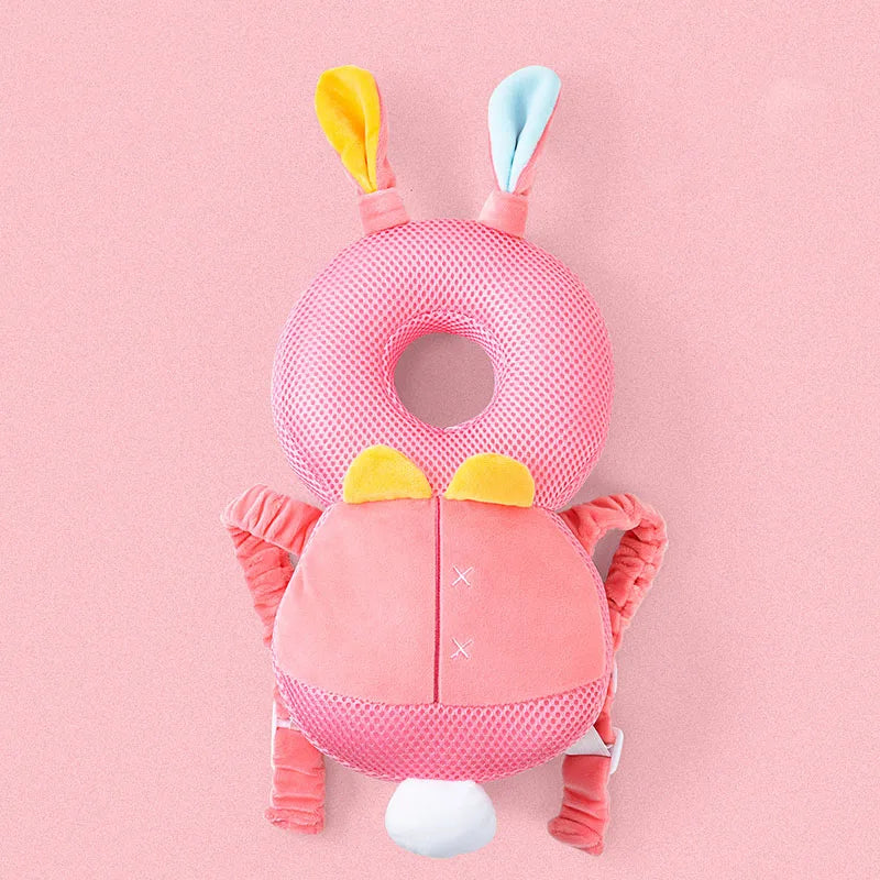 A pink soft baby head protector pillow with yellow and blue ear accents and adjustable straps.