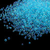A pile of small, iridescent blue and purple glass bubble beads scattered against a black background.