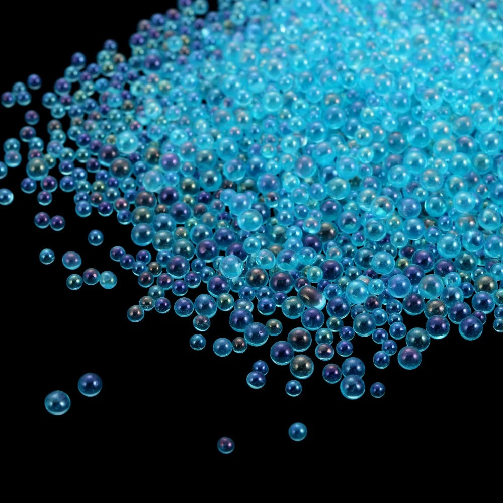 A pile of small, iridescent blue and purple glass bubble beads scattered against a black background.