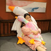 A woman is cuddling with an oversized white goose plush pillow and a pink and yellow goose plush pillow.