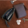 A dark brown leather coin purse with a zipper and a small leather tool are displayed on a brown surface.