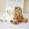 Two soft white and brown teddy bears with gold ribbons sitting in front of a bag labeled Le sac en papier
