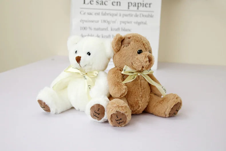 Two soft white and brown teddy bears with gold ribbons sitting in front of a bag labeled Le sac en papier