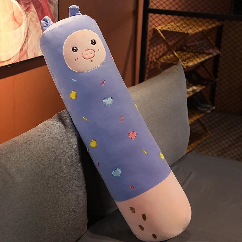 A soft, elongated plush pillow shaped like a baby with rosy cheeks and colorful dots, resting on a gray sofa.