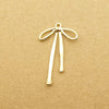 A gold-colored alloy bow charm with a loop and hanging strands is displayed on brown paper.