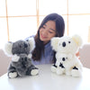 A young woman smiles while holding two fluffy white koala plush toys on a white table.