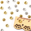 A collection of small silver and gold hollow flower bead caps for jewelry making displayed on a wooden ruler.